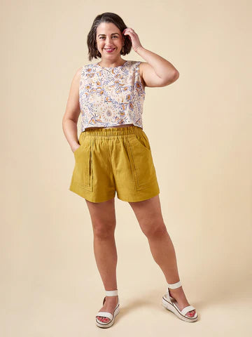 Woman wearing a floral top and yellow shorts made using Sepia Pants and Shorts sewing patternagainst a beige background