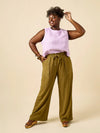 Woman wearing a light purple sleeveless top and olive green wide-leg pants made using Sepia Pants and Shorts sewing pattern on a beige background