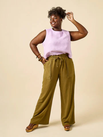 Woman wearing a light purple sleeveless top and olive green wide-leg pants made using Sepia Pants and Shorts sewing pattern on a beige background