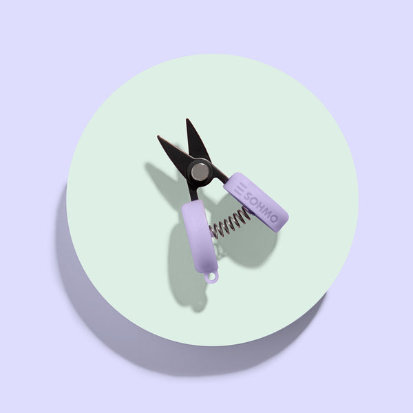 Pet nail clippers with purple handle on a light green circle against a light purple background