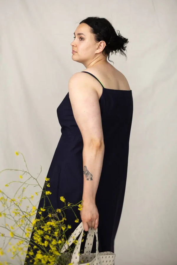 Woman in a black dress holding a white bag against a neutral background with yellow flowers.