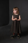 Young girl in a polka dot dress made using trapezette girls dress sewing pattern standing against a dark background