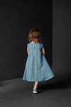 Child wearing a blue striped dress made using trapezette girls dress sewing pattern against a black background