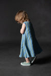 Child wearing a blue striped dressmade using trapezette girls dress sewing patternagainst a dark background