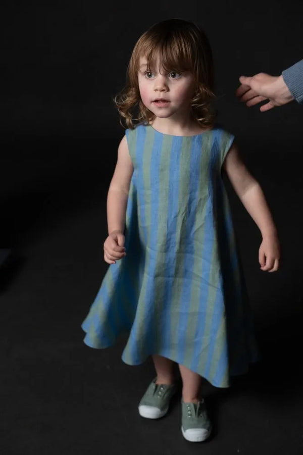 Young girl wearing a blue and green striped dressmade using trapezette girls dress sewing pattern against a dark background