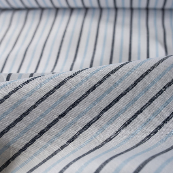 Alternating sky blue and midnight vertical stripes on a white linen blend fabric, with a natural slub texture and soft appearance.