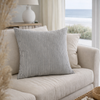 Charcoal Striped pillow on a beige sofa in a living room with a lamp and window in the background.