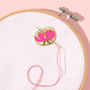 Embroidery hoop with pink thread and a floral embroidery design on a light pink background