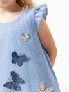 Close-up of a child's blue dressmade using andie kids dress sewing pattern with butterfly appliqués on a white background