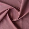 Close-up of Blush Terra linen–cotton blend fabric in a muted dusky rose tone, plain weave texture, 136 GSM with folds