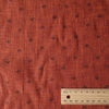 Close-up of burnt orange linen fabric with chocolate damask-style floral print and textured slubby yarn-dyed fibers