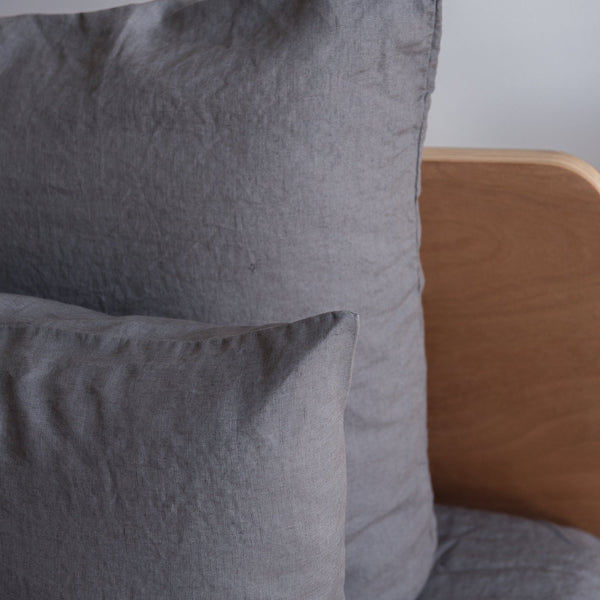 Charcoal grey European linen textured pillows on a bed with a wooden headboard.