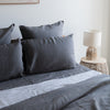 Gray bedding set on a bed with a lamp and side table in the background.