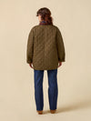 Person wearing a quilted jacket and blue jeans on a beige background