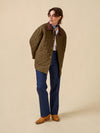 Person wearing a quilted green jacket on a beige background