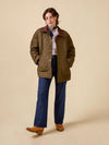 Person wearing a quilted jacket, blue jeans, and brown shoes on a beige background