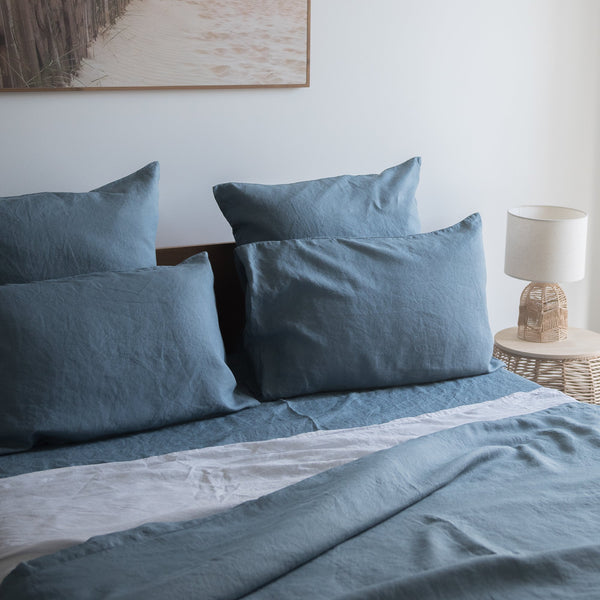 Blue bedding set on a bed with a lamp and painting in the background