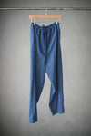 Blue The 101 Trouser Sewing Pattern by Merchant & Mills – relaxed drawstring linen trousers for beginners hanging on a wooden hanger against a gray background