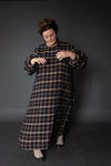 Person wearing a long plaid dress against a dark background