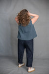 Person wearing a blue top and dark pantsmade using The Eve Trouser Sewing Pattern by Merchant & Mills – cropped tapered trousers with side zip and pleats against a gray background