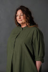 Woman wearing a green dress made using The Niven Sewing Pattern by Merchant & Millsagainst a grey background