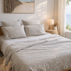 Neatly made bed with Natural linen flat sheet soft beige bedding in a bright bedroom.