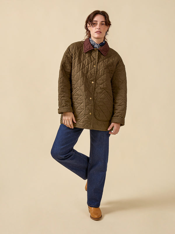 Person wearing a brown quilted jacket and blue jeans on a beige background