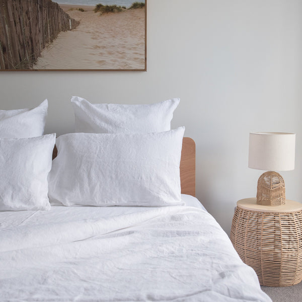 Neatly made bed with white linen bedding and pillows in a bedroom setting.