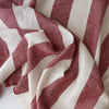 A close-up of draped striped Rosewood Broadstripe linen fabric with alternating wide bands of dusty rose red and off-white, showing a textured woven surface.