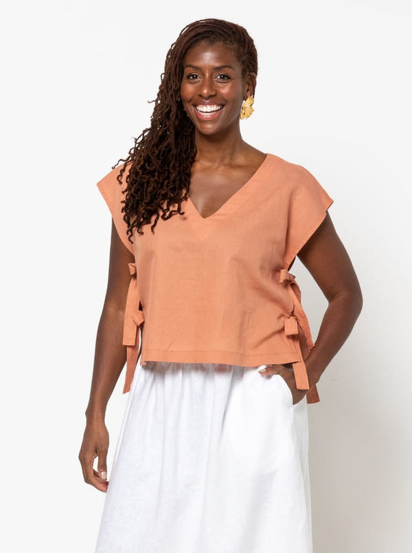 Woman wearing a peach top made using Rumi Top Sewing Pattern with ruffle details on a white background