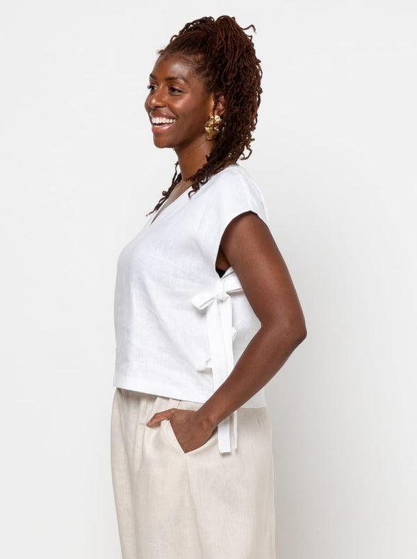 Woman wearing a white top made using Rumi Top Sewing Pattern with a tie detail on a plain background