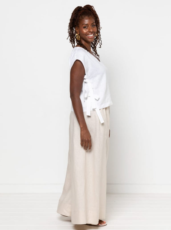 Woman wearing a white sleeveless top made using Rumi Top Sewing Patternand beige pants against a white background
