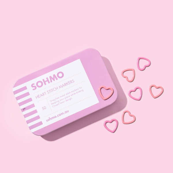 Pink SOHMO heart stitch markers in a tin on a pink background