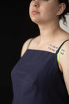 Woman wearing a dark blue dress with visible tattoos on her neck against a black background