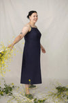 A woman modeling a sleeveless navy blue midi dress, standing in a studio with a white backdrop and decorative yellow flowers.