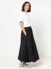 Woman wearing a white top and black skirt made using Sophia Woven Bubble Skirt and Pant sewing pattern on a white background