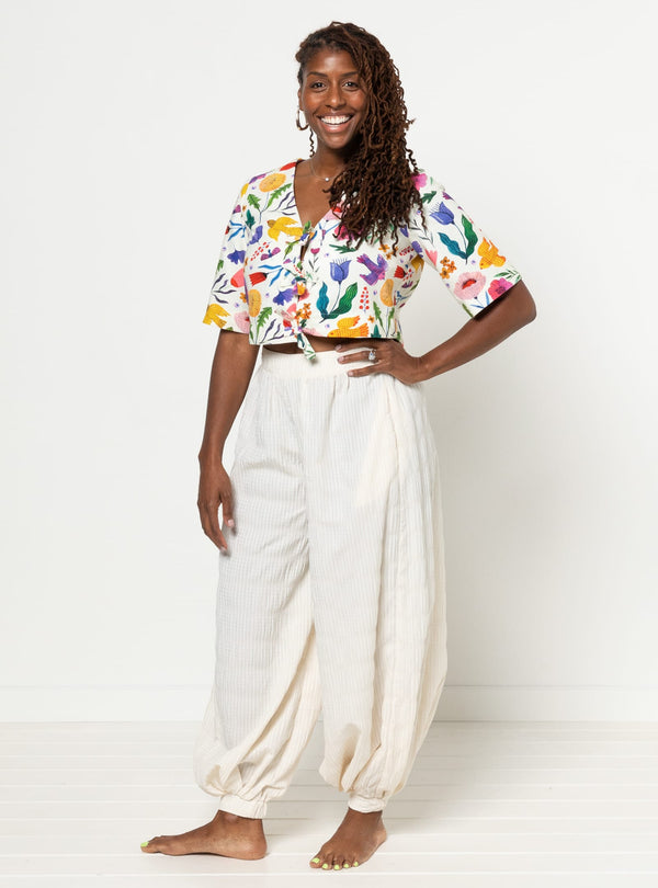 Woman wearing a colorful floral blouse made using Sophia Woven Bubble Skirt and Pant sewing patternand white pants on a white background