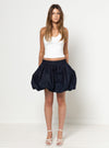 Woman wearing a white top and black skirt made using Sophia Woven Bubble Skirt and Pant sewing pattern on a white background