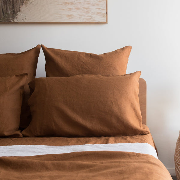 Tobacco brown linen fitted sheet on a bed with a neutral wall and framed picture in the background